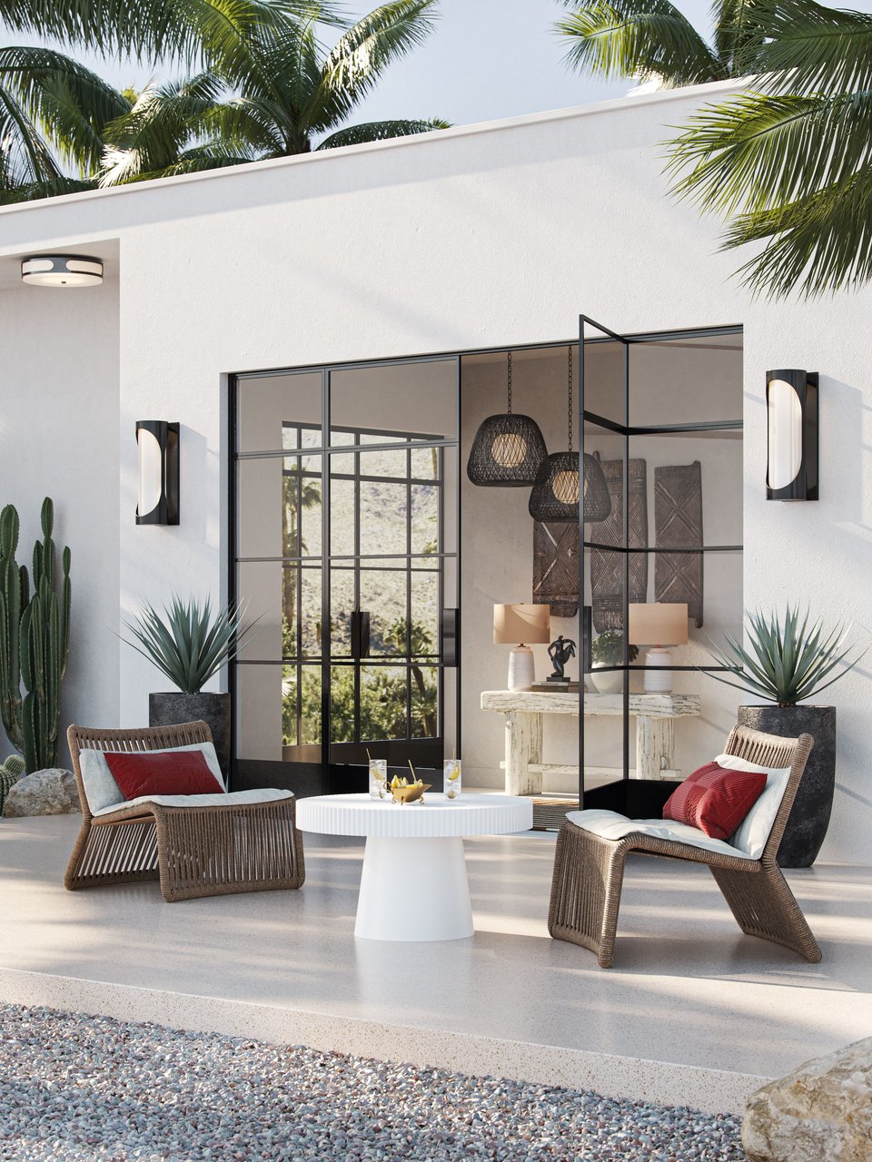 CGI visualization of black outdoor wall sconces, woven lounge chairs, and a white pedestal table on a modern desert patio with wicker pendant lights, ceramic table lamps, carved wall panels, and a rustic console visible through steel-framed glass doors